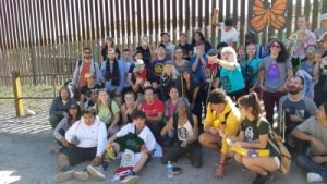 group of people at the boarder wall with a monarch butterfly sign (symbol of migrant support)