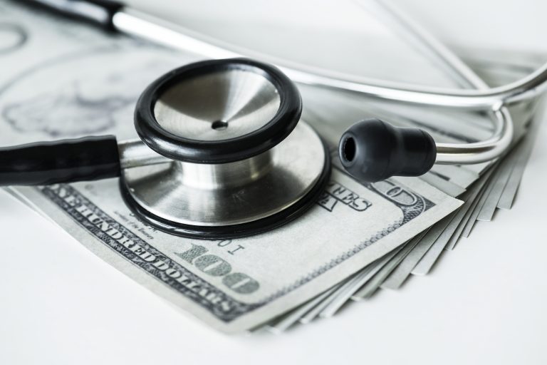 close-up of stethoscope lying on cash, with a $100 bill visible